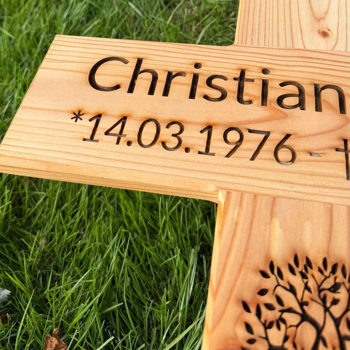 Personalisiertes Grabkreuz aus Holz mit Gravur von Name und Lebensdaten, Detailaufnahme im Gras