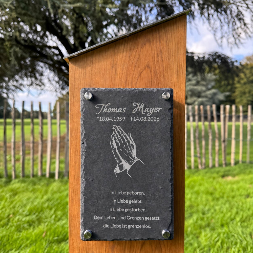 Nahaufnahme einer Holz-Grabstele mit betenden Händen, Namen, Lebensdaten und persönlichem Gedenkspruch auf Schiefer.