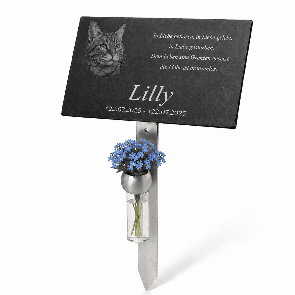 Personalisierte Gedenktafel für eine Katze mit graviertem Katzenporträt, dem Namen ‚Lilly‘, vierzeiligem Trauerspruch und Datumsangabe. Die schwarze Tafel ist auf einem Metallstab befestigt und mit einer Vase voller blauer Vergissmeinnicht geschmückt.