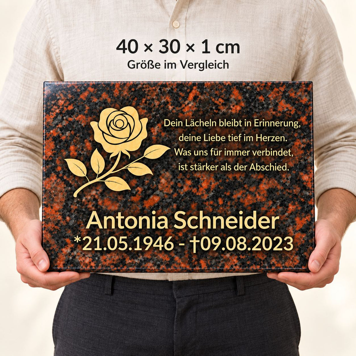Mann hält eine personalisierte Tan-Brown-Granitgedenktafel mit goldener Rose und Beschriftung vor dem Körper zum Größenvergleich, Maße 40 × 30 × 1 cm.