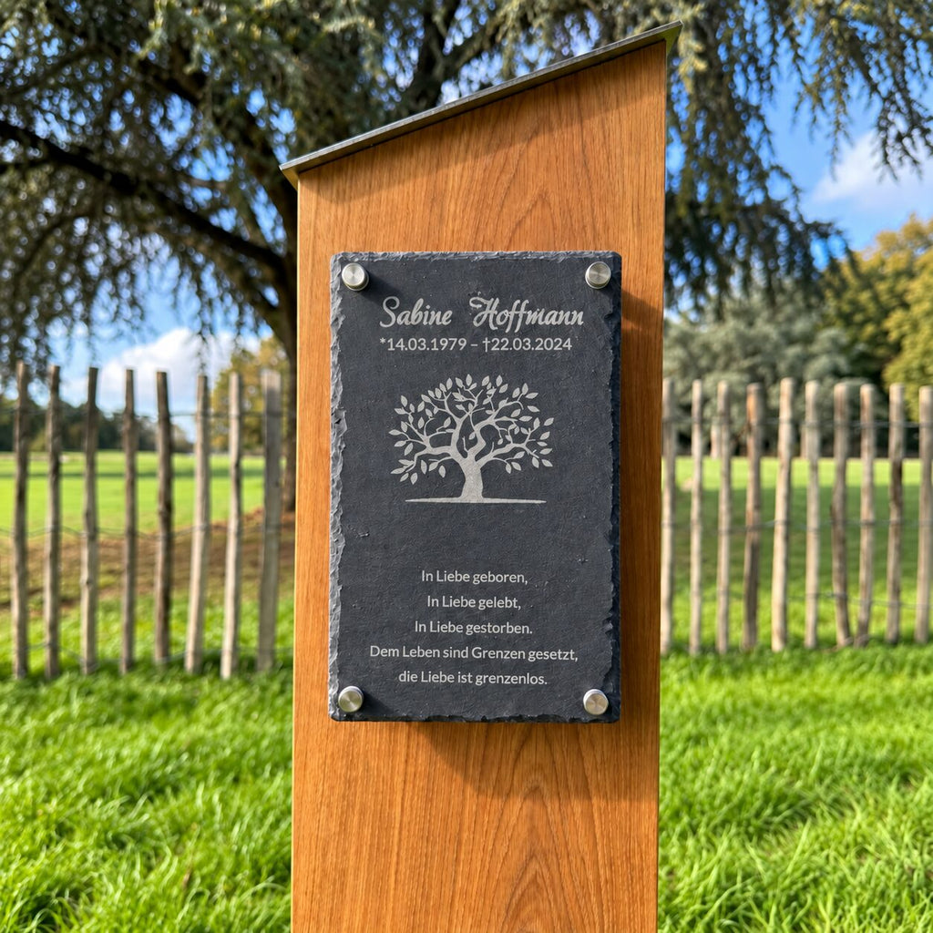 Grabstele aus Holz mit Schiefertafel, Lebensbaummotiv sowie graviertem Namen, Lebensdaten und Gedenkspruch im Garten.